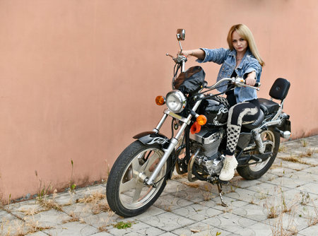 Beautiful woman in black leggings and short denim jacket rides her beautiful chopper motorcycle on a...