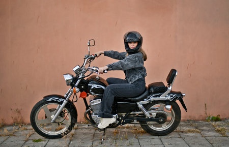 Woman in black denim suit and black helmet riding her chopper motorcycle on sunny summer day.
