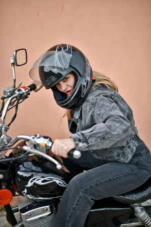 Beautiful woman in black denim suit and black helmet riding her beautiful chopper motorcycle on...