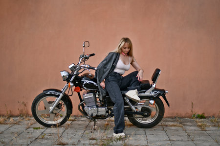Beautiful woman in black denim suit and white top riding her chopper motorcycle on sunny summer day.の写真素材