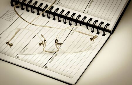 Reading glasses sitting on top of an opened daily plannerの写真素材
