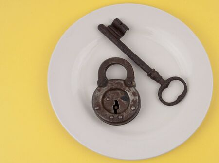 An old key and lock on a  white dinner plate with a yellow backgroundの写真素材