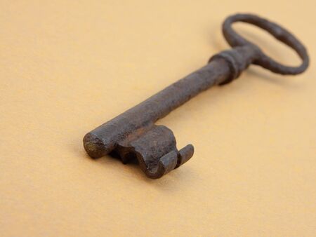 A close up shot of a worn old key with a tan backgroundの写真素材