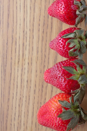 Four red strawberries lined to the right on woodの写真素材