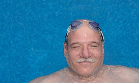 Man relaxing and smiling in the pool with goggles on top of his headの写真素材