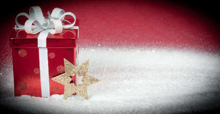 A red gift box and gold star sitting in snow with a red backgroundの写真素材