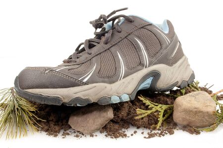 Side view of sneaker on top of rocks, dirt and green leaves isolated on whiteの写真素材