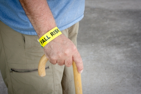 Fall risk bracelet around an elderly man's wrist while walking with a wooden caneの写真素材