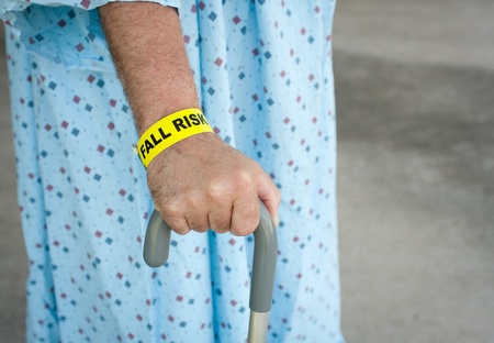An elderly man wearing a fall risk bracelet around his wrist at the hospital. Wearing a blue gown...