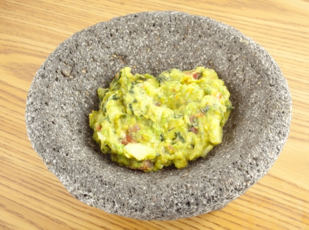 A molcajete mortar bowl filled with guacamole on a wooden tableの写真素材