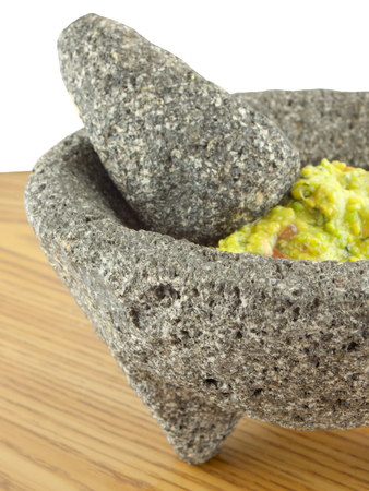 Molcajete mortar bowl and pestle filled with guacamole on a wooden tableの写真素材