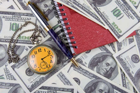 Pocket watch, notebook and pen on a stack of dollars, reflecting time and money の写真素材