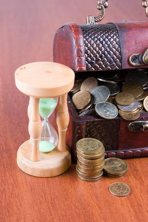 Open chest with coins and  hourglass on a wooden surface close-up