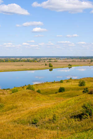Beautiful river and yellow meadow under the summer sky