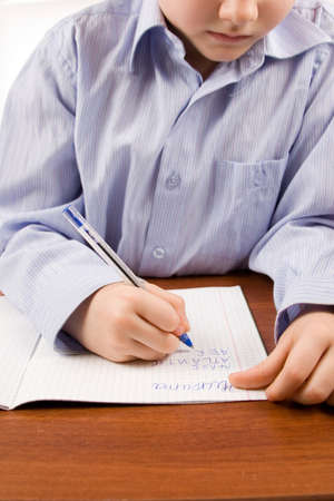 Boy does homework on a table, isolated on a white background