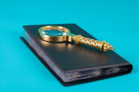 Magnifying glass and  album with a collection of coins on a blue background close upの写真素材