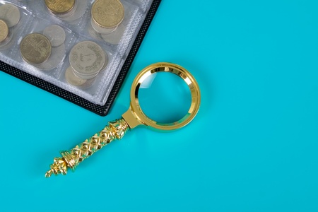 Magnifying glass and  album with a collection of coins on a blue background close up