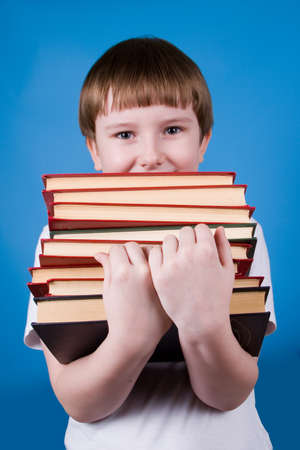 Boy with  pile of books on a blue backgroundの写真素材