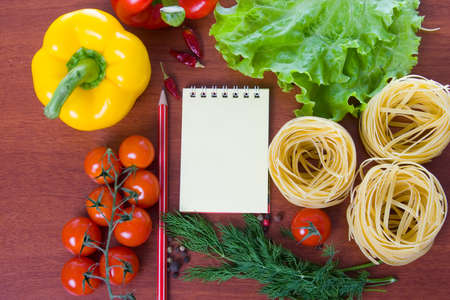 Fresh vegetables,pasta and a notebook on a wooden tableの写真素材