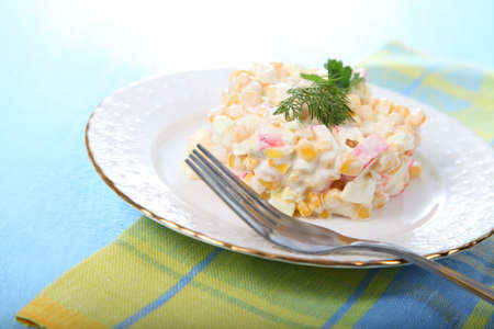 Salad from crab sticks with corn in a white plate on a wooden tableの写真素材