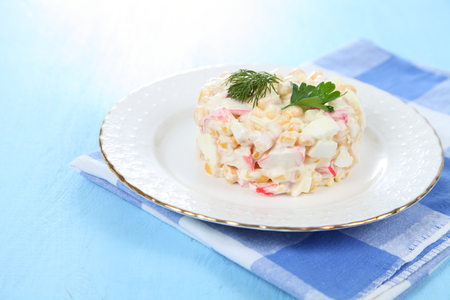 Salad from crab sticks with corn in a white plate on a wooden tableの写真素材