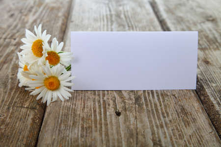 Beautiful chamomiles and greeting card on a blue wooden table