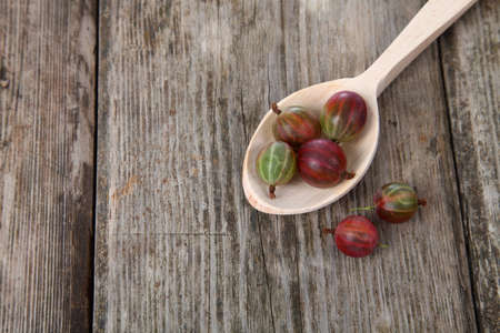 Ripe gooseberries in a wooden spoon on the tableの写真素材