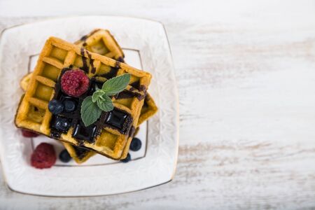 Delicious waffle with berries and chocolate on wooden table. Belgian waffles with raspberries, blueberries and mint, covered with liquid chocolate.の写真素材