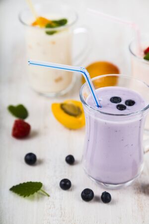 Smoothies or yogurt with fresh berries on a wooden table. Milkshakes with raspberries, blueberries, apricots and mint leaves.の写真素材