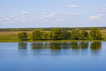Beautiful landscape with  river and  blue sky with clouds. Trees on the river bank reflected in the...