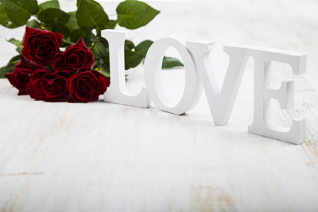 Frame of red roses and  word "Love" on a wooden background. Greeting card with Valentine's Day, Birthday or Wedding.の写真素材