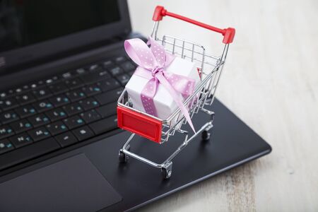 Shopping cart with gift box on laptop. Concept of shopping online. Buying gifts for the holidays online.の写真素材