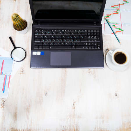 Workplace of  businessman with a laptop and business papers. On the table are coffee, laptop, magnifier, graphics and cactusの写真素材