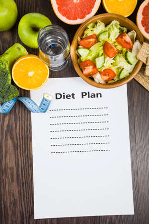 Food and sheet of paper with a diet plan on a dark wooden table. Concept of diet and healthy lifestyle.の写真素材