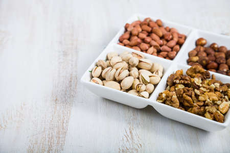 Nuts in a plate on a light wooden table. Different kinds of tasty and healthy nuts.の写真素材