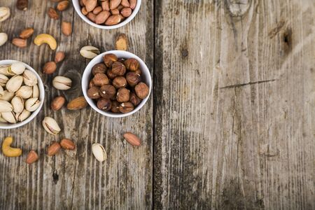 White bowls with nuts on a  wooden table. Different kinds of tasty and healthy nuts. Top viewの写真素材