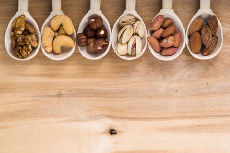 Nuts in a wooden spoons on a  wooden table. Different kinds of tasty and healthy nuts.の写真素材