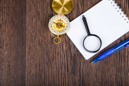 Compass, magnifying glass and  notebook on a wooden table. The concept of travel around the world and tourism.の写真素材