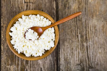 Cottage cheese in a wooden bowl and spoon on the table. Healthy food for breakfast.の写真素材