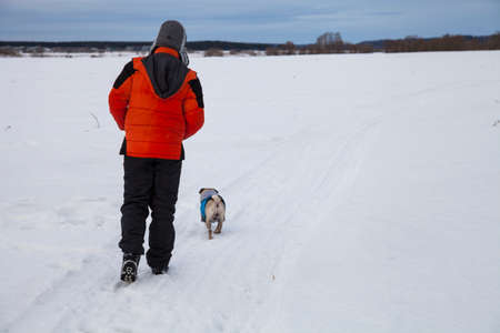 Boy and dog walking in winter. Teenager and a pug walk along a snow-covered field.の写真素材