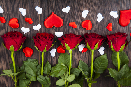 Red roses and hearts on a wooden background. Greeting card with Valentine's Day, Birthday or Wedding.の写真素材