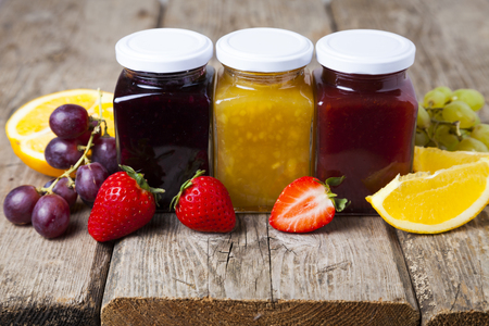 Three jars with jam on a wooden background. Delicious dessert and fresh fruits close-up.の写真素材