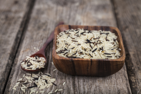 Mixture of different varieties of rice in a bowl on a wooden background. Ingredient for a healthy diet.の写真素材