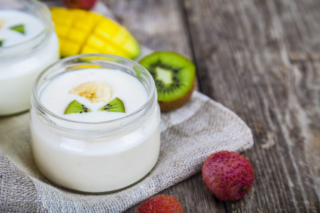 Yogurt with tropical fruits on a wooden background. Tasty breakfast. Healthy eating.の写真素材