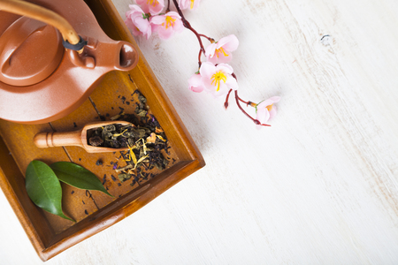Ceramic teapot, tea leaves and sakura on a wooden tray, top view. Oriental tea.の写真素材