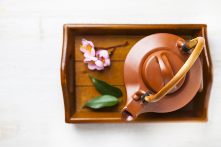 Ceramic teapot, tea leaves and sakura on a wooden tray, top view. Oriental tea.の写真素材
