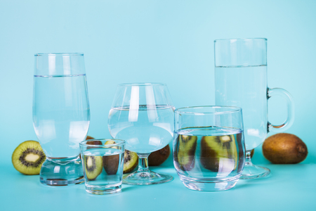 Refreshing  cold water with kiwi on a blue background. Transparent water in different glasses with fruit reflection.の写真素材