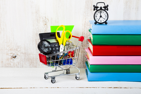 Items for school in a shopping cart,alarm clock and books on a wooden background. Concept of buying items for school. Back to school.の写真素材