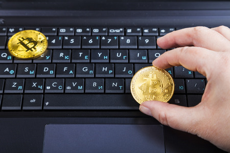 Female hand holds bitcoin on a laptop background. Electronic currency.の写真素材