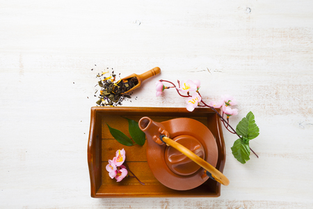 Ceramic teapot, tea leaves and sakura on a wooden tray, top view. Oriental tea.の写真素材